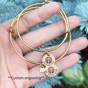Op de afbeelding: Twee gouden armbandjes met een bedel met de tekst "Psalm 34:8 Wees met God" met een kruis en een hartbedel.