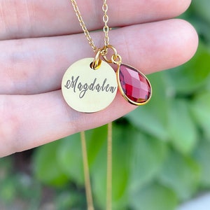 May include: Gold necklace with a round pendant that says "Magdalen" and a small teardrop-shaped red gemstone.