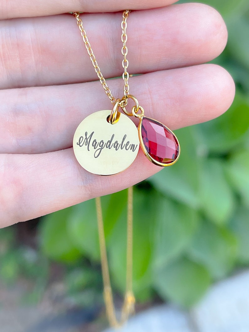 May include: Gold necklace with a round pendant that says "Magdalen" and a small teardrop-shaped red gemstone.
