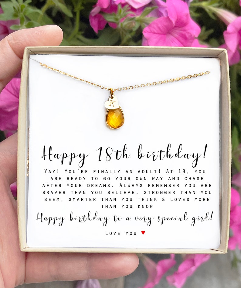 May include: A gold necklace with a small heart charm and a teardrop-shaped amber stone pendant. The necklace is in a white box with a message that reads "Happy 18th birthday! YAY! You're finally an adult! At 18, you are ready to go your own way and chase after your dreams. Always remember you are braver than you believe, stronger than you seem, smarter than you think & loved more than you know. Happy birthday to a very special girl! LOVE YOU".