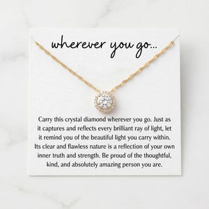 May include: A gold necklace featuring a crystal pendant with a halo of smaller crystals. The necklace is presented on a white card with the words "wherever you go...".