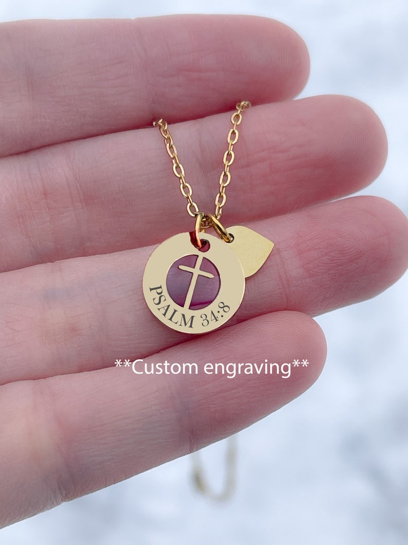 Op de afbeelding: Gouden ketting met een ronde hanger met een kruis en de tekst "PSALM 34:8". De hanger is bevestigd aan een klein hartvormig bedeltje. **Aangepaste gravure** staat onder de hanger.