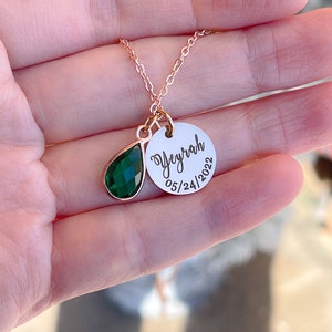 May include: A gold necklace with a green teardrop-shaped gemstone and a round pendant with the name "Veyrah" and the date "05/24/2022" engraved on it.