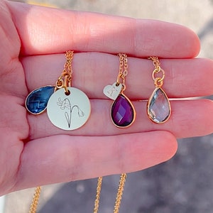 May include: Gold-toned necklaces with pendant charms. One necklace features a blue teardrop-shaped charm. Another has a round charm with a floral design. A third necklace has a purple teardrop charm, and the last has a light blue teardrop charm.