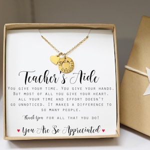 May include: A gold necklace with a heart charm and a round charm featuring an apple and the text "MS GREGORIA" inside. The necklace is presented in a box with a card that reads "Teacher's Aide You give your time. You give your hands. But most of all you give your heart. All your time and effort doesn't go unnoticed. It makes a difference to so many people. Thank you for all that you do! You Are So Appreciated"