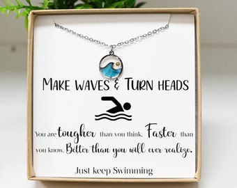 May include: A silver necklace with a blue wave charm and the text "MAKE WAVES & TURN HEADS". The necklace is in a box with the text "You are tougher than you think. Faster than you know. Better than you will ever realize. Just keep Swimming."