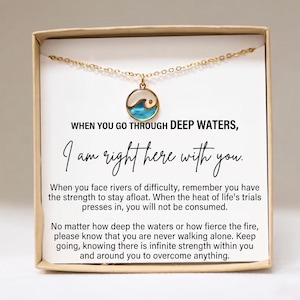 May include: A gold-tone chain necklace with a circular pendant featuring a blue and white wave design. The necklace is displayed on a white card inside a tan box, printed with the text: WHEN YOU GO THROUGH DEEP WATERS, I am right here with you.