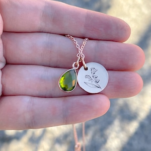 May include: A delicate gold necklace with a green gemstone pendant and a circular pendant with an engraved lily of the valley design.