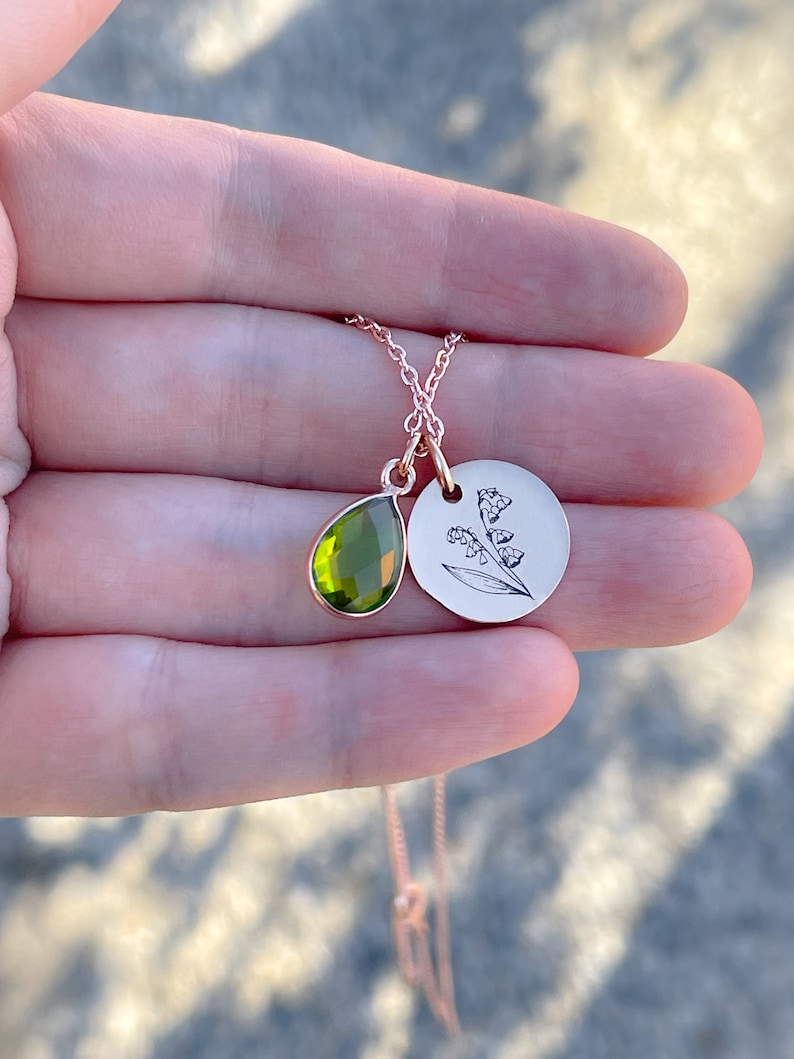 May include: A delicate gold necklace with a green gemstone pendant and a circular pendant with an engraved lily of the valley design.