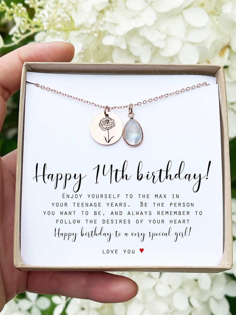 May include: A rose gold necklace with a round pendant engraved with a flower and a teardrop-shaped moonstone charm. The necklace is presented in a gift box with the text "Happy 14th birthday!" and a heartfelt message.