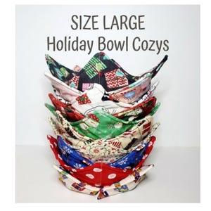 May include: A stack of large fabric bowl cozies featuring various holiday-themed patterns including presents, snowmen, and snowflakes. The text "SIZE LARGE Holiday Bowl Cozys" is printed above the stack in a dark gray sans-serif font.
