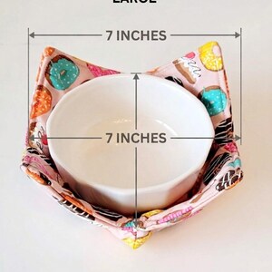 May include: A white ceramic bowl inside a pink fabric bowl cozy. The cozy is patterned with donuts in various colors. The bowl and cozy are each 7 inches in diameter. The word "LARGE" is at the top.