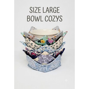 May include: A stack of large fabric bowl cozies featuring various floral and paisley patterns in shades of blue, white, and pink, with a white ceramic bowl nestled inside the top cozy. The text SIZE LARGE BOWL COZYS is printed above the stack.