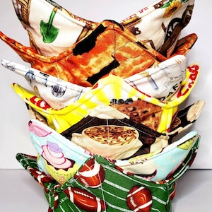 May include: A stack of five colorful fabric bowl cozies. The cozies are made of different fabrics with various patterns, including a green and white football pattern, a blue and white cupcake pattern, a brown and white coffee cup pattern, a yellow and white pattern with the text "Gourmet Market", and a white and brown pattern with a wheelbarrow and a sunflower.