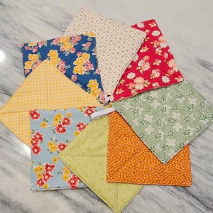 May include: Set of eight colorful fabric pot holders with floral and geometric patterns. The pot holders are made of cotton and have a quilted design.