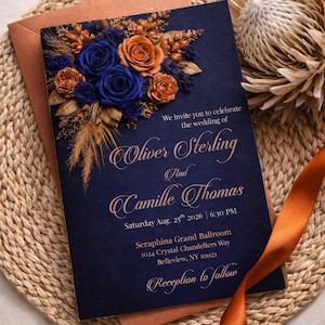 Puede incluir: Invitación de boda azul marino con detalles florales en tonos azules y naranjas. La invitación incluye los nombres de Oliver Sterling y Camille Thomas, la fecha y el lugar de la boda. Un sobre color cobre está detrás de la invitación.