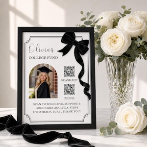 May include: A framed black and white sign with the text "Olivia's COLLEGE FUND" and a photo of a graduate. The sign includes QR codes for CashApp and Zelle, and a black velvet bow. The sign is surrounded by white roses.