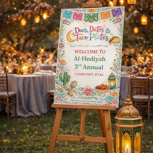 May include: A wooden easel supports a sign with the text "Duas, Dates & Taco Plates" and "Welcome to Al-Hediyah 3rd Annual Community Iftar." The sign is decorated with colourful floral illustrations. A lit lantern is placed nearby.