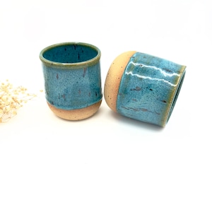 May include: Two handmade ceramic mugs with a teal glaze and a speckled brown rim.