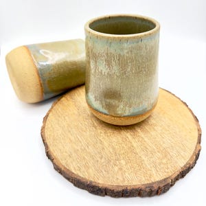 Könnte beinhalten: Ein Set aus drei Keramikbechern mit gesprenkelter, matter Oberfläche. Jeder Becher hat eine andere Farbe: hellblau, cremefarben und grau. Die Becher haben ein schlichtes, modernes Design und einen bequemen Griff.