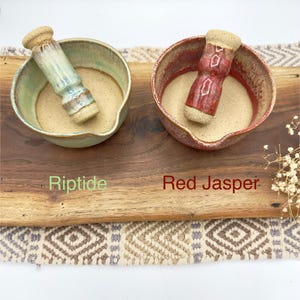 K&ouml;nnte beinhalten: Zwei M&ouml;rser- und St&ouml;&szlig;el-Sets aus Keramik. Ein Set hat eine hellblaue und gr&uuml;ne Glasur mit der Aufschrift Riptide, das andere eine rote und braune Glasur mit der Aufschrift Red Jasper. Beide Schalen haben ein beiges Inneres und einen Ausguss.