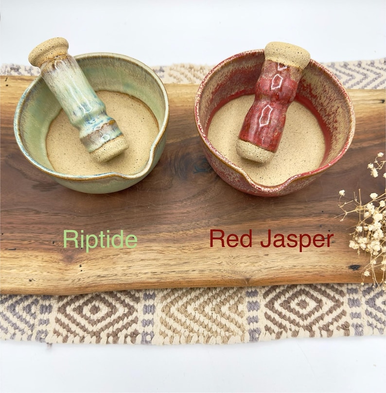 K&ouml;nnte beinhalten: Zwei M&ouml;rser- und St&ouml;&szlig;el-Sets aus Keramik. Ein Set hat eine hellblaue und gr&uuml;ne Glasur mit der Aufschrift Riptide, das andere eine rote und braune Glasur mit der Aufschrift Red Jasper. Beide Schalen haben ein beiges Inneres und einen Ausguss.