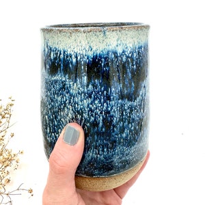 May include: A blue and white ceramic mug with a speckled glaze. The mug has a brown rim and base.