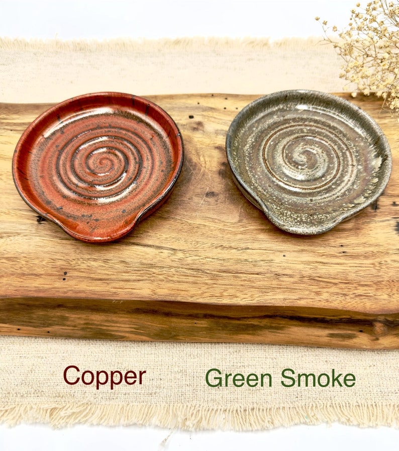 May include: Two ceramic spoon rests, one in a copper glaze and the other in a green smoke glaze. Both have a spiral design.