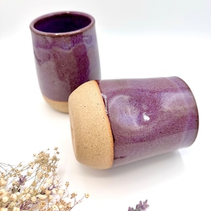 Könnte beinhalten: Zwei violette Keramikbecher mit einem hellbraunen Rand. Die Becher stehen auf einer weißen Oberfläche.