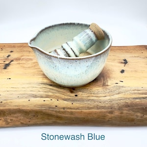 K&ouml;nnte beinhalten: Ein M&ouml;rser mit St&ouml;&szlig;el aus Keramik mit einer gesprenkelten, steingrau-blauen und wei&szlig;en Glasur sowie einem braunen Rand. Die Schale hat einen kleinen Ausgie&szlig;er und der St&ouml;&szlig;el ein strukturiertes, unglasiertes beiges Ende. Der Text Stonewash Blue steht darunter.