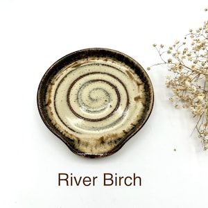 May include: A ceramic spoon rest with a brown and white swirl design. The spoon rest has a slight curve to it and is perfect for holding spoons, spatulas, and other utensils.