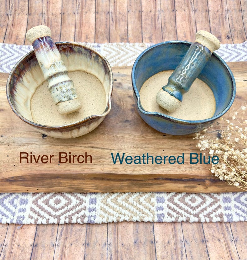 K&ouml;nnte beinhalten: Zwei M&ouml;rser- und St&ouml;&szlig;el-Sets aus Keramik. Das linke Set ist mit River Birch beschriftet und besteht aus einer cremefarbenen und braun glasierten Schale mit passendem St&ouml;&szlig;el. Das rechte Set ist mit Weathered Blue beschriftet und hat eine blaue Schale.
