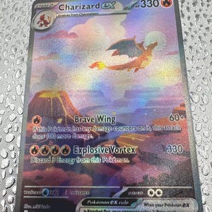 May include: A Charizard ex trading card with 330 HP, featuring a holographic illustration of a flying Charizard over a volcanic landscape. The card displays the attacks Brave Wing and Explosive Vortex, along with game rules and set information.