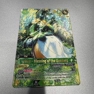May include: A rectangular trading card featuring a green and gold forest illustration with a central character wearing a white dress and flower crown. The text reads Ayleen - Blessing of the Goddess, Lucky Pal, and includes game mechanics and stats.