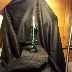 May include: A green glass oil lamp with a wick burning on a black fabric background.