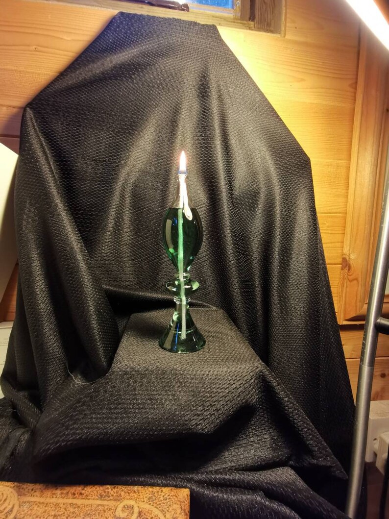 May include: A green glass oil lamp with a wick burning on a black fabric background.