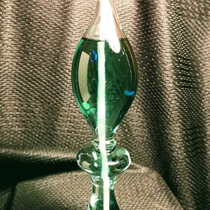 May include: A green glass oil lamp with a white wick and a clear glass reservoir. The lamp is lit and the flame is visible.