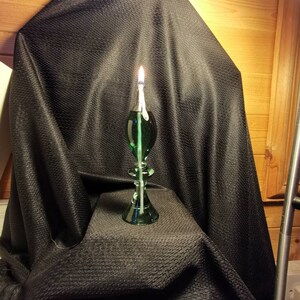 May include: A green glass oil lamp with a wick burning on a black fabric background.