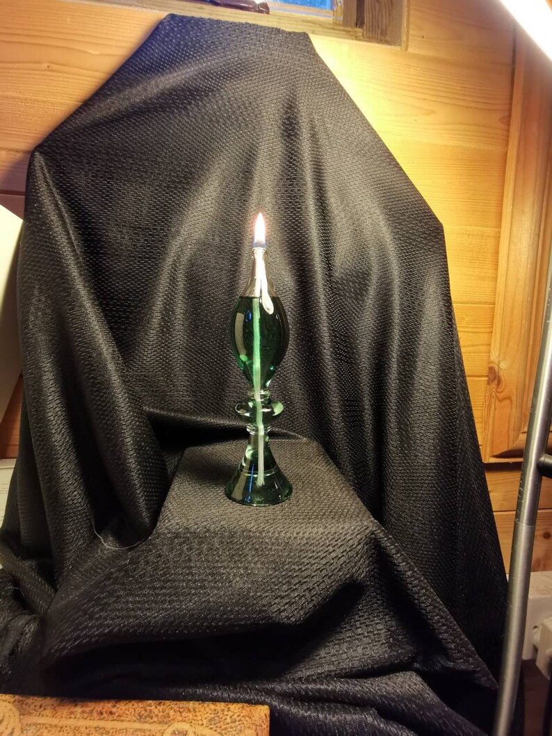 May include: A green glass oil lamp with a wick burning on a black fabric background.