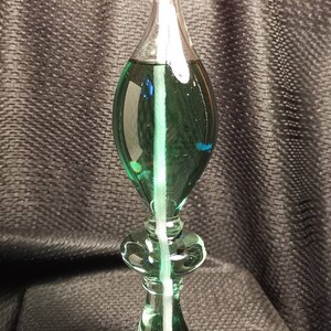 May include: A green glass oil lamp with a white wick and a clear glass reservoir. The lamp is lit and the flame is visible.