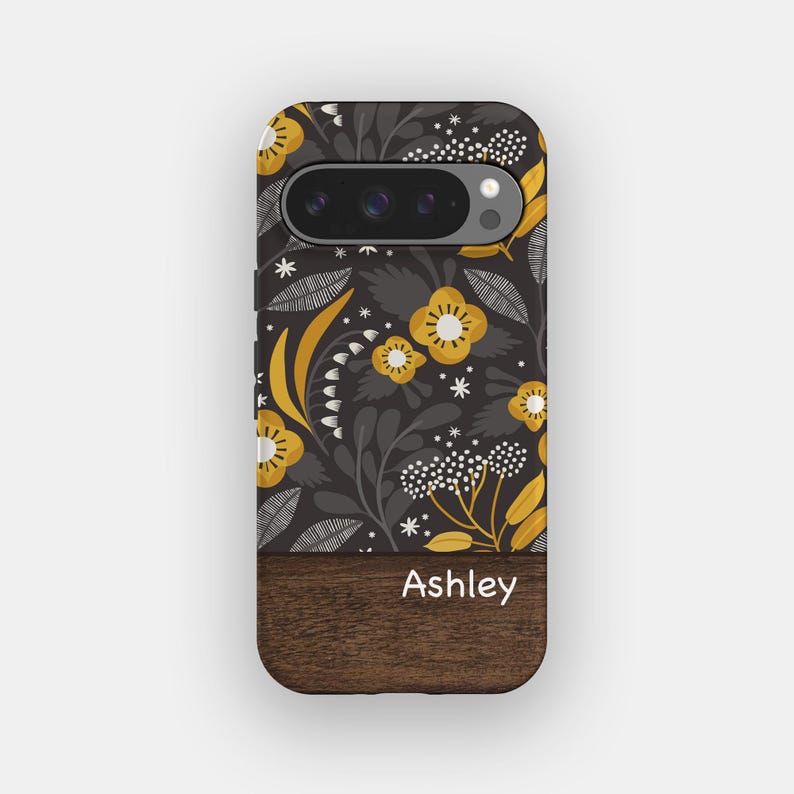 May include: A phone case featuring a dark gray background with a mustard yellow and white floral pattern. The bottom section has a dark brown wood grain texture with the name Ashley printed in white text across the center of the wood panel.