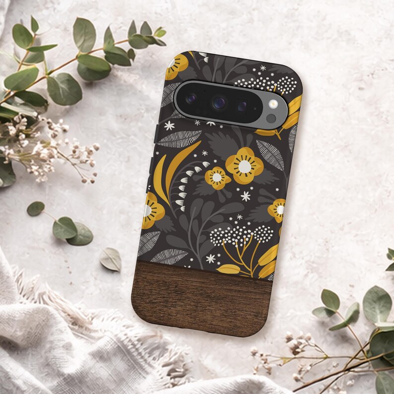 May include: A smartphone case featuring a dark gray background with a repeating pattern of yellow flowers, white star-like accents, and gray leaves. The bottom section of the case is made of a solid dark brown wood with a visible horizontal grain.