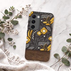 May include: A rectangular phone case featuring a dark gray background with a mustard yellow and white floral pattern on the top portion and a solid dark brown wood grain texture on the bottom portion, including a triple camera cutout.