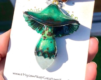 May include: A green and gold mushroom pendant necklace with a clear quartz crystal at the bottom. The necklace is made of leather cord and wooden beads. The pendant is attached to the cord with a gold chain. The pendant is about 2 inches tall. The necklace is available for purchase on Etsy.