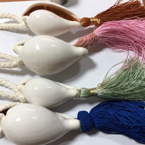 Può includere: Quattro conchiglie bianche con nappe di diversi colori. Le nappe sono blu, verdi, rosa e marroni.