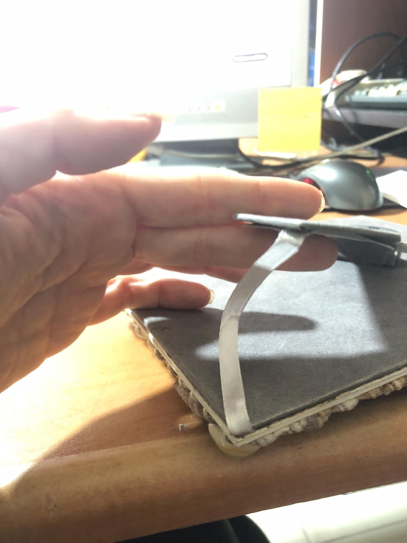 K&ouml;nnte beinhalten: Eine graue, rechteckige Fliese mit einem wei&szlig;en Klebestreifen. Die Fliese hat eine strukturierte Oberfl&auml;che und wird von einer Hand gehalten. Die Kanten der Fliese sind mit einem hellfarbigen Material versehen.