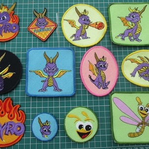 May include: A collection of eleven embroidered patches featuring the purple dragon Spyro in various poses, including circular, square, and flame-shaped designs. Several patches display the character breathing fire, while others show the Spyro logo.
