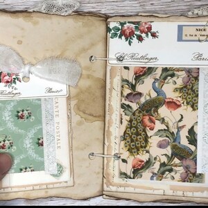 May include: A vintage scrapbook with pages featuring floral and peacock designs. The pages are decorated with lace and paper scraps. The scrapbook has a worn and aged look.