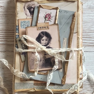 Könnte beinhalten: Ein Stapel alter Umschläge und Papiere, die mit einem Spitzenband zusammengebunden sind. Die Papiere sind gealtert und haben einen abgenutzten Look. Das oberste Papier zeigt ein Schwarzweißporträt einer Frau mit der Nummer "B6765" darauf gedruckt.