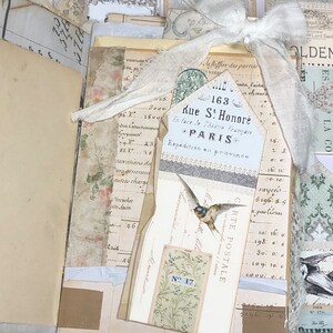May include: A vintage postcard with a white lace bow and a bird illustration. The postcard has the text "163 Rue St. Honor&eacute; * PARIS * Exp&eacute;dition en province" and "CARTE POSTALE" printed on it. The postcard is decorated with a floral pattern and a small tag with the number "17" printed on it.